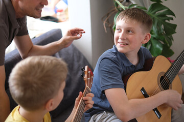 Happy father and sons playing guitars together and smiling at home