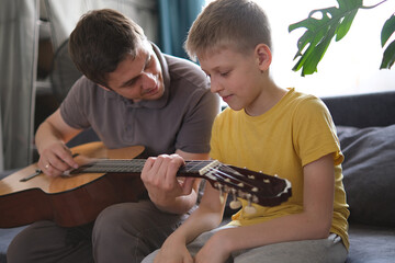 Father teaching his son to play guitar at home, family bonding