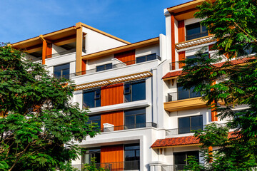 Modern apartment building with orange accents surrounded by trees under blue sky