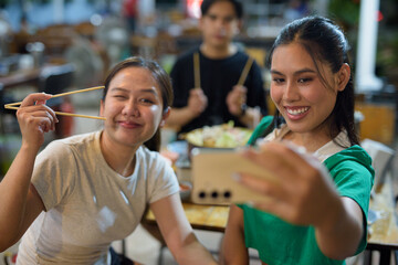 Woman taking selfie while eating Mu Kratha with friends at night