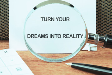 TURN YOUR DREAMS INTO REALITY words focused on the notebook through a magnifying glass