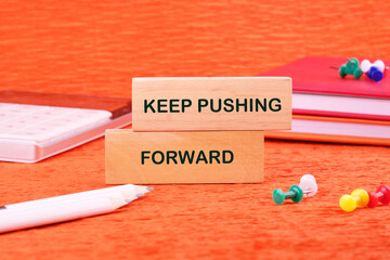 Concept text KEEP PUSHING FORWARD made of wooden blocks on an orange background with stationery...