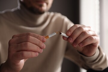 Man holding broken cigarette on blurred background, closeup. Stop smoking