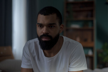 Sadness and despair overwhelm shirtless black man sitting on bed