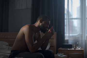 Black guy lights cigarette embodying emotional pain and struggle in dark room
