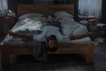 Stressed young man lies on untidy bed. Serious mental health problems