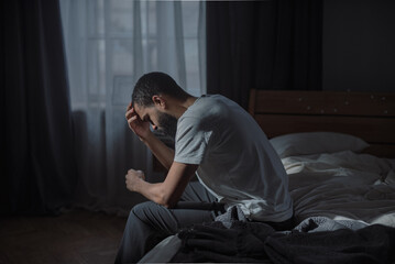 Young African American man experiences profound emotional pain sitting on bed