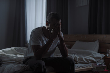 Depressed African American man cries sitting on messy bed in room