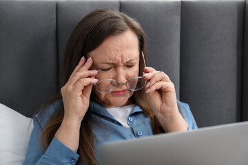 Woman with vision problem using laptop on bed at home