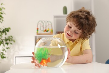 Little boy with goldfish in aquarium on table at home