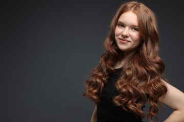 Naklejka premium Portrait of beautiful teenage girl with healthy wavy hair on dark grey background. Space for text