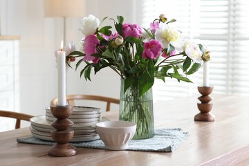 Dining table with beautiful flowers and dishware in room. Interior design