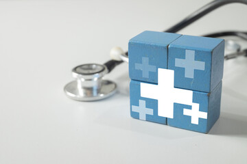 Blue wooden blocks forming a medical cross with a stethoscope in the background. Concept for a...