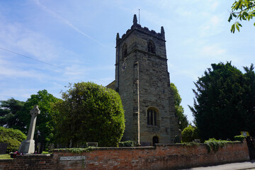 Nottingham, Nottinghamshire, England &ndash; June 18 2025: Traditional stone church with a tall square bell tower and Celtic-style cross monument in lush village setting.