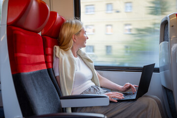 Woman working on laptop while traveling by train in daylight, concept of remote work and travel