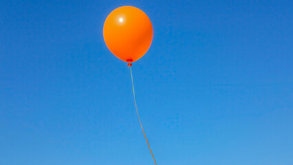 A single orange balloon floats in the clear blue sky. The image symbolizes lightness, freedom and striving upward. Contrasting colors create a bright and minimalistic visual impression.