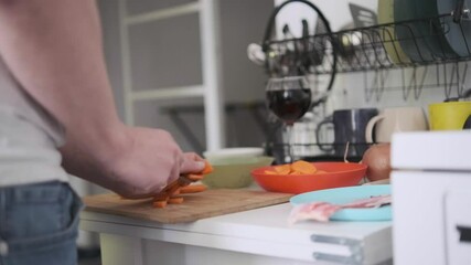 Man slicing carrot on wooden cutting board, preparing fresh ingredients at home kitchen table - Powered by Adobe