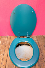 Top view of a sawdust composting toilet with a blue plastic seat and open lid, installed on a wooden floor against a pink wall. Eco-friendly and waterless sanitation solution