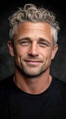 The attractive man, in his thirties, showcases stylish grayish hair and a warm smile. He stands against a dark background, exuding confidence and approachability in this striking portrait