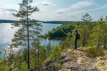 The tourist man standing at edge a rock and looking into the distance at the lake. The concept of win travel.