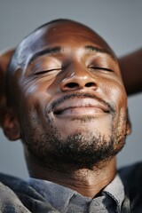 A close-up portrait of a smiling Black man with his eyes closed. His relaxed demeanor exudes tranquility and joy. The soft lighting highlights his features and the textures of his skin.