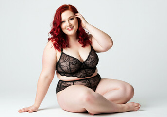 Portrait of a beautiful oversize woman in lingerie sitting on white background. Plus size woman in underwear looking at camera with hand on head