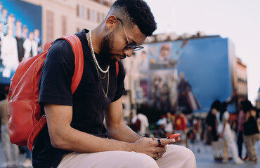 Concentrated African-American man in urban setting checking smartphone, dressed in casual clothing...