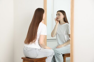 Beautiful woman looking at herself in mirror indoors