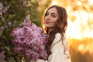 Fototapeta premium Beautiful woman with bouquet of lilac flowers outdoors in morning