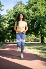 Fototapeta premium Happy sportswoman running outdoors in the park, vertical photo, front view