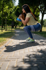 Beautiful smiling woman doing kettlebell squat exercise in the park, side view, vertical photo
