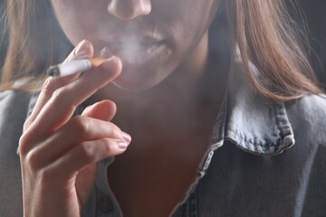 Woman in shirt smoking cigarette on dark background, closeup. Bad habit