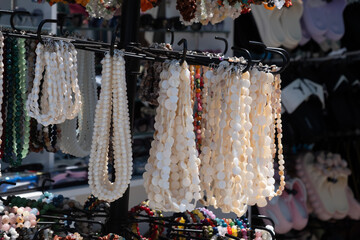 Strings of white shell beads hang on a rotating rack at an outdoor market stall, sunlit against a...