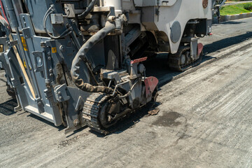 Heavy machinery with track undercarriage, rotating drum grinds and removes worn asphalt layer, preparing roadbed for resurfacing, enhancing road durability, transportation infrastructure upgrades