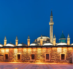The Mevlana Museum, mausoleum of Rumi, illuminated at dusk in Konya, Turkey. Historic landmark with its famous green dome and minaret against a deep blue sky
