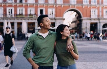 Interracial couple exploring historic square arm in arm, looking around with awe and admiration,...
