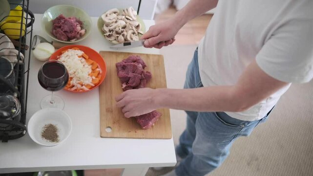 Man cutting fresh beef into cubes, preparing ingredients for cooking at home. Homemade Beef bourguignon. Part of series