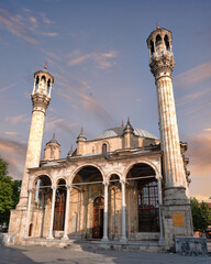 Low-angle view of the historic Aziziye Mosque in Konya, Turkey. Ottoman architecture with two ornate minarets stands against a beautiful sunset sky