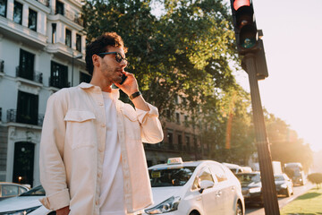 stylish young male entrepreneur, dressed in white shirt and glasses, takes a business call in a...