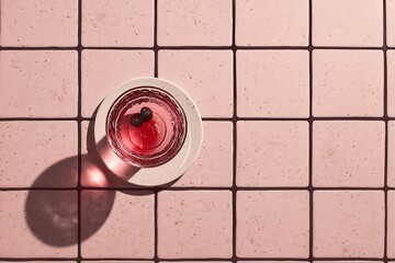 A pink and black tiled floor with a cocktail on top, a flat lay composition, with a minimal, grainy film aesthetic.