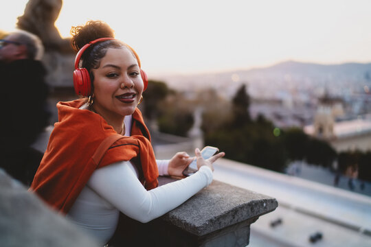 young woman with wireless headphones and smartphone enjoys digital content, streaming music or watching video. Female engaging in a virtual meeting or voice messaging with mobile phone device - Powered by Adobe