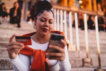 Stylish young Latina woman completes a secure mobile transaction while sitting on city steps. With...