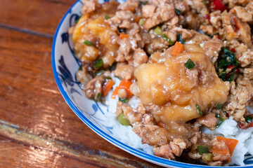 A Thai rice dish topped with stir-fried minced pork, vegetables, and battered fried egg, served in...