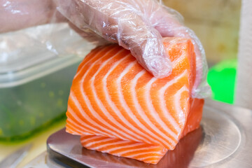 Fresh raw salmon fillet being held with a gloved hand on a stainless steel scale, ready for...
