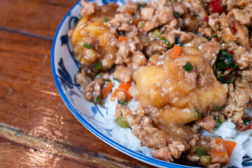 A Thai rice dish topped with stir-fried minced pork, vegetables, and battered fried egg, served in...