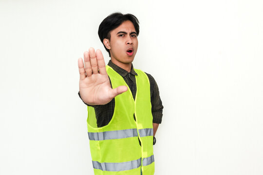 Portrait of a serious Asian construction worker showing a stop hand gesture on an isolated white background