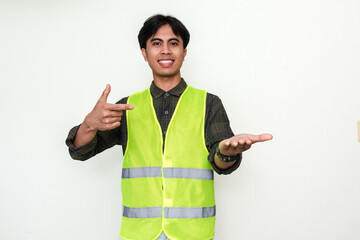 Portrait of a smiling Asian construction worker pointing at his open palm, standing against white...