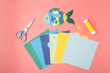 Colorful paper fish DIY project with scissors and glue on pink background for preschool learning,...