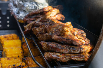 Grill is full of meat and corn. The meat is cooked and the corn is grilled. The grill is on a table.