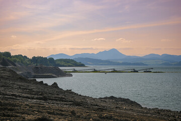 Industrial conveyors extracting resources by a lake at sunset, highlighting the impact of mining on...